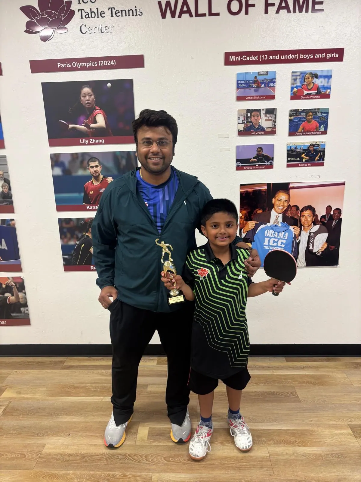 Pannag Mahesh holding his bat and trophy beside Subham Kundu in front of the ICC Table Tennis Center Wall of Fame