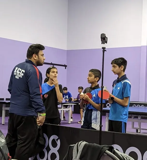 Subham Kundu in an ICC jacket briefing three players between matches